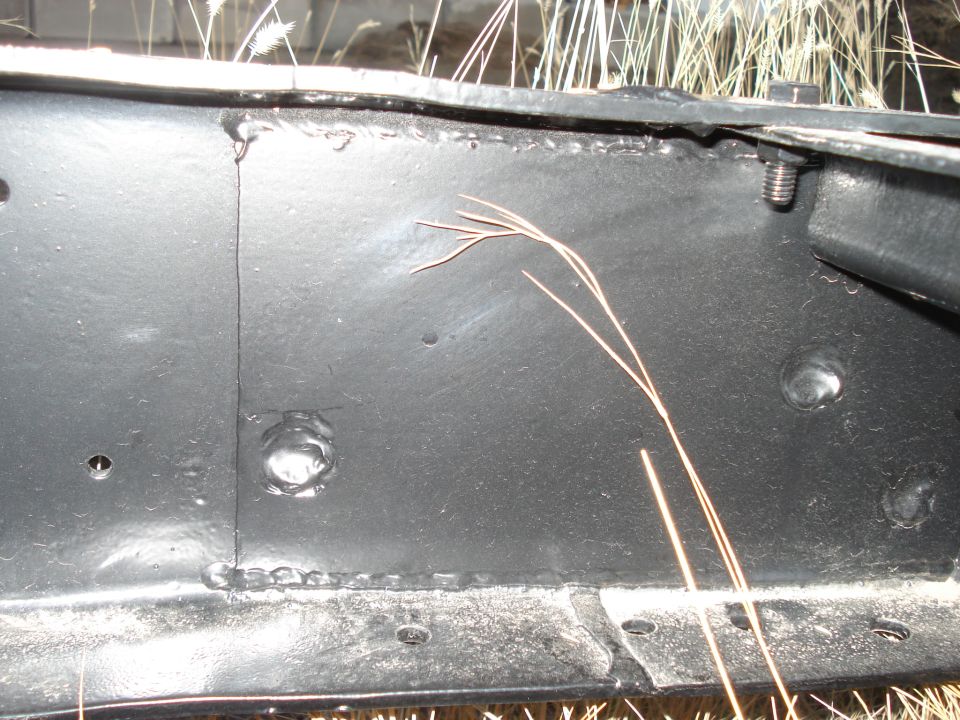 Close-up of a black metal truck frame with visible welds and a bolt