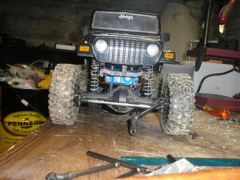 1994 Ford Escort - A black Jeep Wrangler toy is shown from the front, with its suspension and large tires prominently displayed on a workbench.