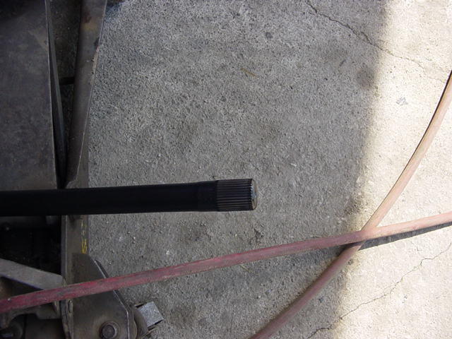 Splined end of an axle shaft lying on concrete next to a floor jack and red hose