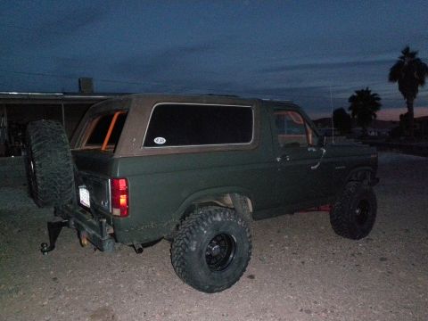 1982 Ford Bronco - Rear view of a green 1982 Ford Bronco, a spare tire mounted on the rear bumper and aftermarket wheels.