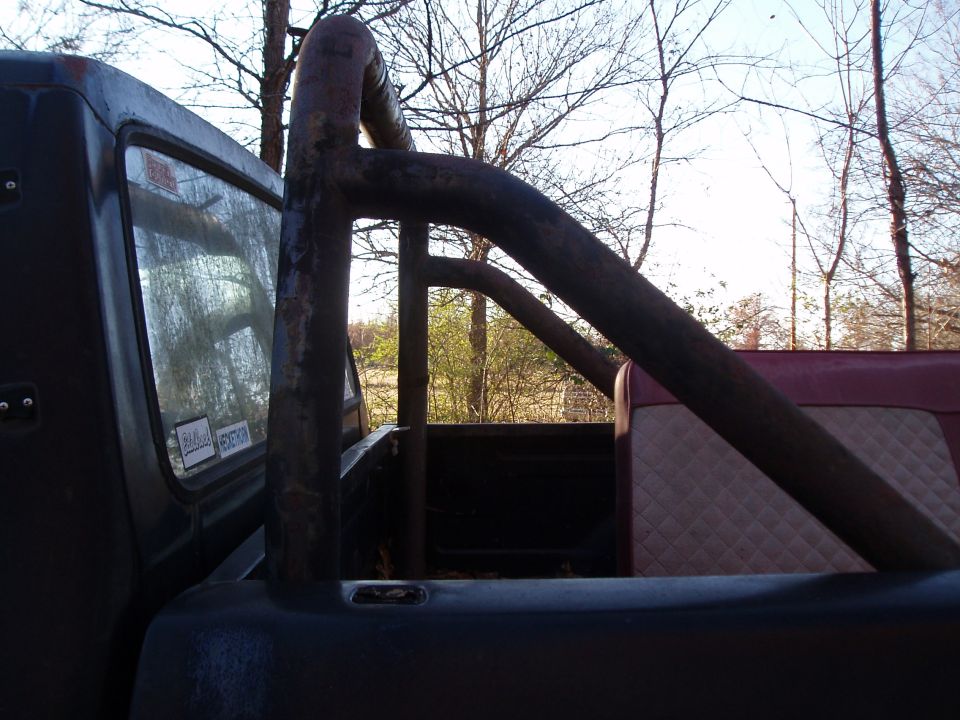 Black truck bed with a rusty roll cage and quilted red and tan seat visible