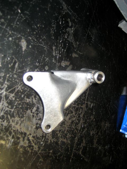 1996 Ford Bronco - A metal bracket is shown against a dark, scratched surface, with a blue tube of lubricant visible to the right.