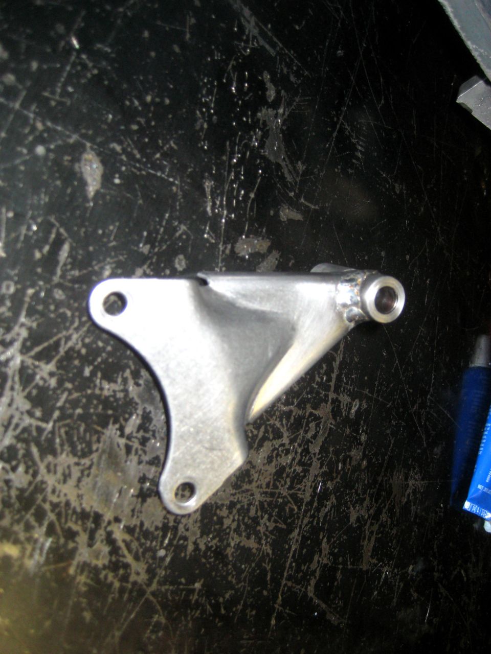 Metal bracket with two mounting holes and a threaded insert, on a scratched black surface