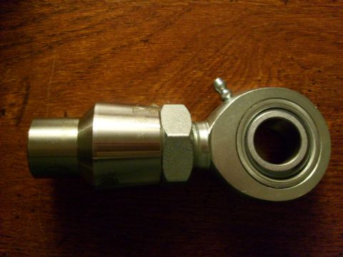 1986 Ford Bronco - A close-up view of a metal rod end bearing with a grease fitting, placed on a wooden background.