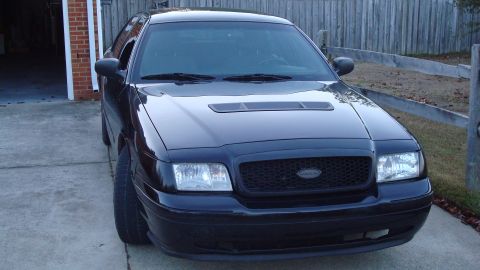 2004 Ford Crown Victoria - A black Ford Crown Victoria is parked in front of a garage and wooden fence.