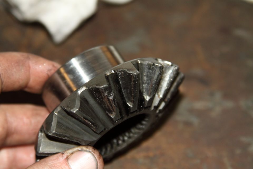 Hand holding a chipped differential pinion bevel gear over a workbench