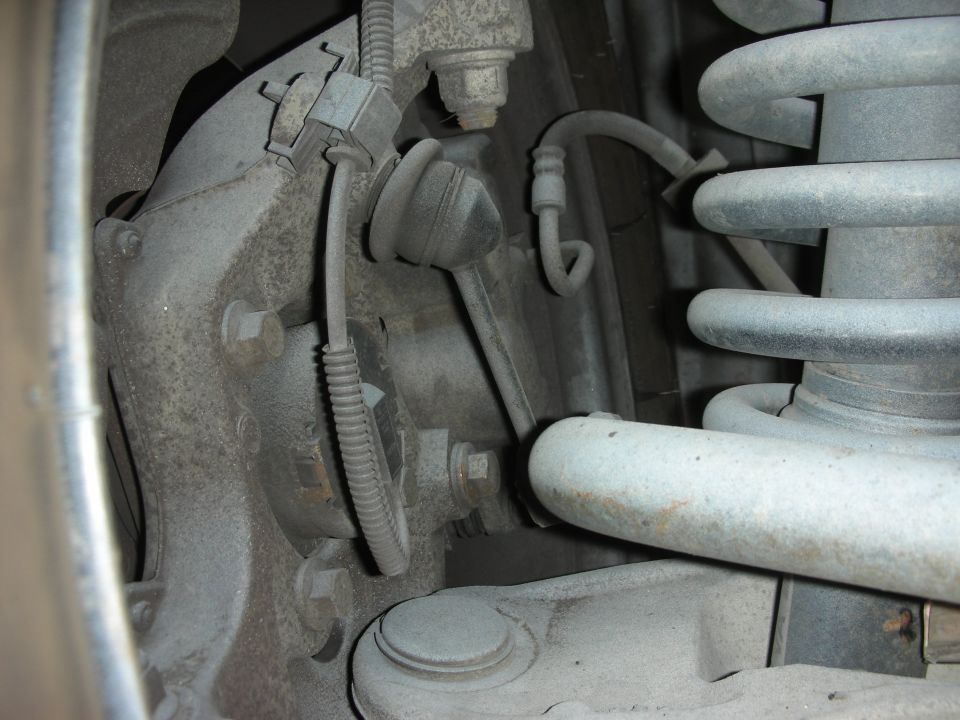 Close-up of dusty suspension parts including a coil spring, sway bar link, and brake line