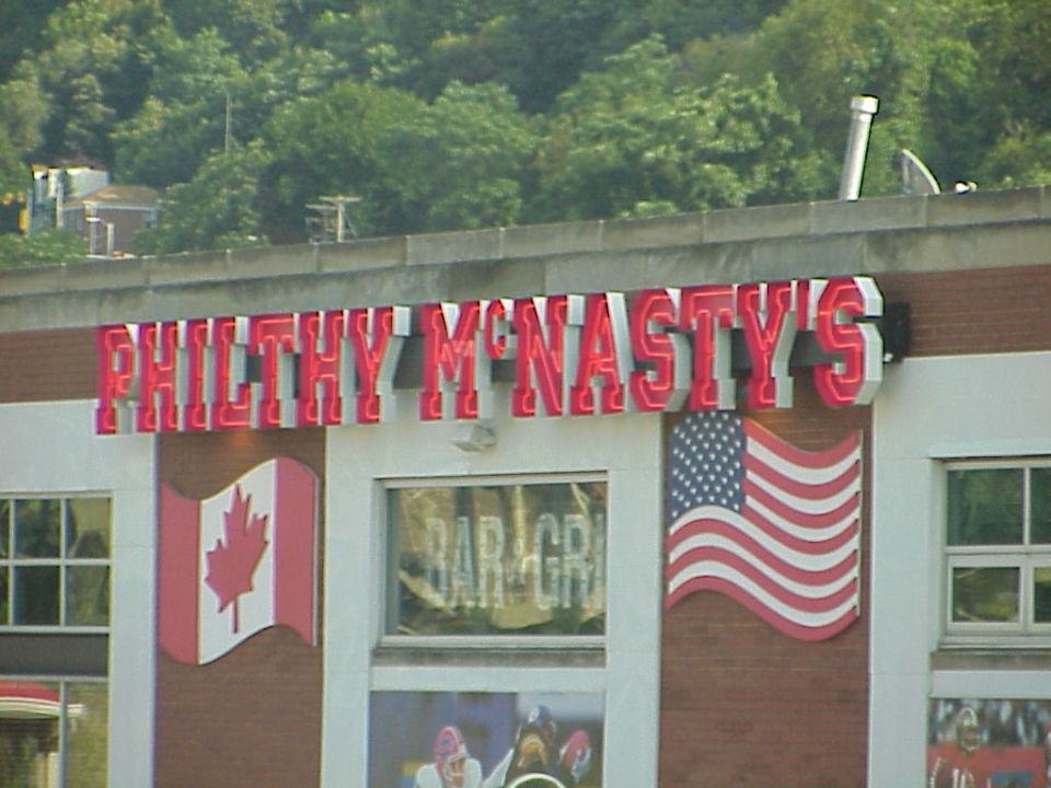 Building facade with neon sign 'PHILTHY MCNASTY'S', Canadian and American flags, and 'BAR GRILL' text
