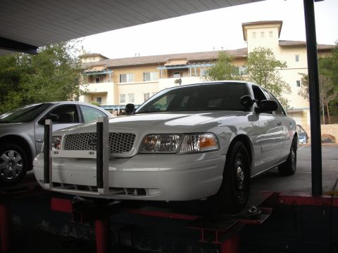 2004 Ford Crown Victoria - A white 2004 Ford Crown Victoria police car is shown on a lift, with a push bumper installed on the front.