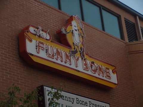 1998 Ford Taurus - A neon sign for the Funny Bone comedy club features a hot dog mascot and the club's name in illuminated lettering.