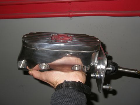 1990 Ford Bronco - A chrome brake master cylinder with a ribbed lid is held in a person's hand.