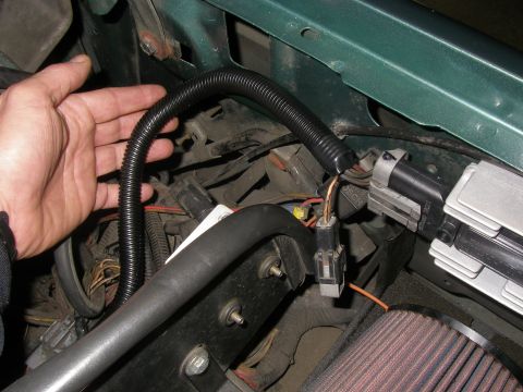 1990 Ford Bronco - Close-up of engine bay wiring, showing a hand manipulating a protective conduit over electrical cables.