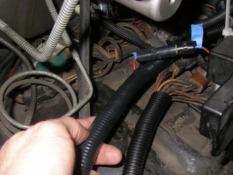 1990 Ford Bronco - Close-up of an engine bay showing a hand near a wiring harness and a connector secured with blue tape.