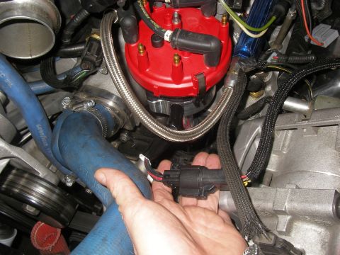 1990 Ford Bronco - Close-up of engine components, focusing on a hand connecting a sensor in the ignition system.