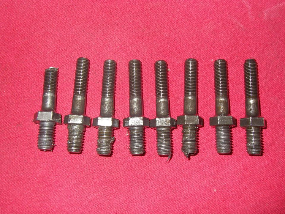 Eight used rocker arm studs arranged in a row on red cloth
