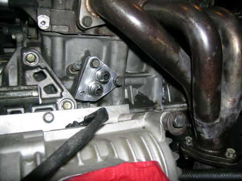 1995 Ford Probe - Close-up view of an engine showing an aftermarket oil line adapter plate and exhaust manifold.