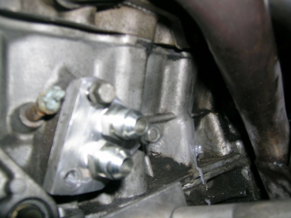 Close-up of an aftermarket oil cooler adapter bolted to an engine block, with metal lines attached