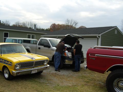 2007 Ford Mustang - Two men are working on a silver pickup truck, with a yellow classic car in the foreground.