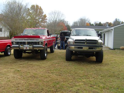 2007 Ford Mustang - Two lifted trucks, a red Ford F-Series and a silver Dodge Ram, are parked outside on a grassy area with a house and garage in the backgroun…