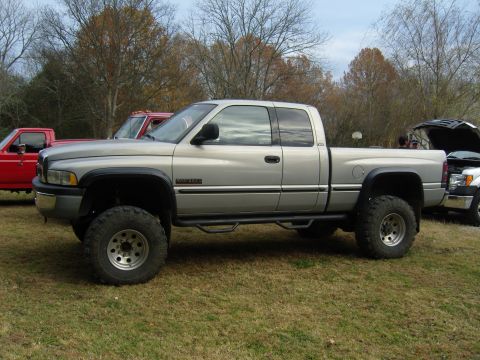 2007 Ford Mustang - Silver Dodge Ram pickup truck with lifted suspension parked on grass. Another truck is visible in the background.