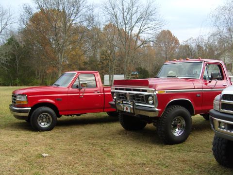 2007 Ford Mustang - Two red pickup trucks are parked on a grassy area with trees in the background.