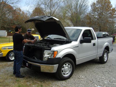 2007 Ford Mustang - Two men inspect the engine of a silver Ford F-150 pickup truck parked outdoors.