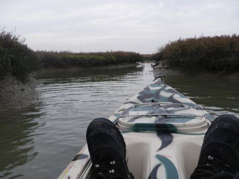 1991 Ford Bronco - A person's feet are visible in a camouflage kayak as it travels down a narrow waterway surrounded by vegetation.