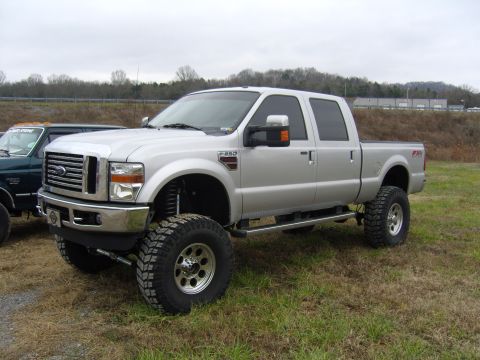2007 Ford Mustang - Lifted silver Ford F-250 Super Duty pickup truck with large off-road tires is parked on grass.