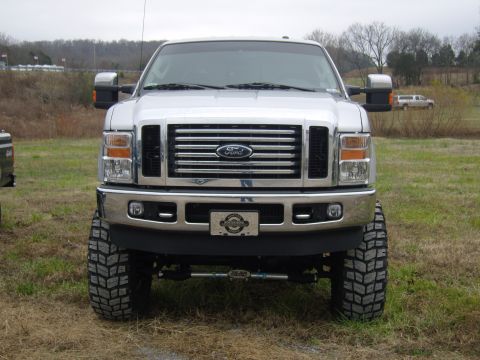 2007 Ford Mustang - This lifted Ford Super Duty truck features a prominent grille and large off-road tires, with another vehicle in the distance.