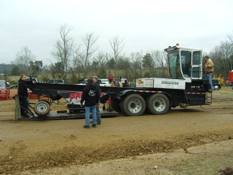 2007 Ford Mustang - A tow truck with a trailer is parked on a dirt track, with several people standing around.