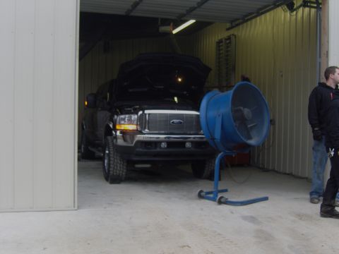 2007 Ford Mustang - A black Ford F-Series truck is parked inside a garage with its hood open, next to a large blue industrial fan.