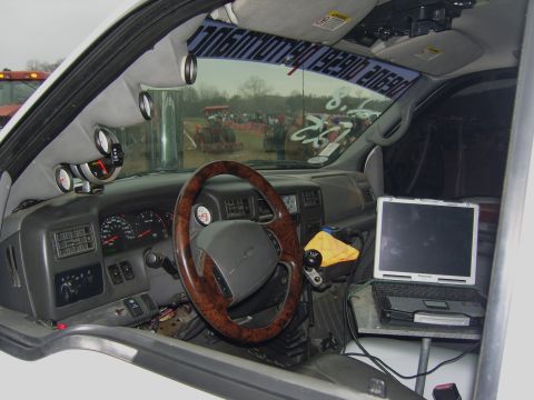 2007 Ford Mustang - The interior of a truck is shown with multiple gauges and a laptop mounted on the dash, with tractors visible through the windshield.