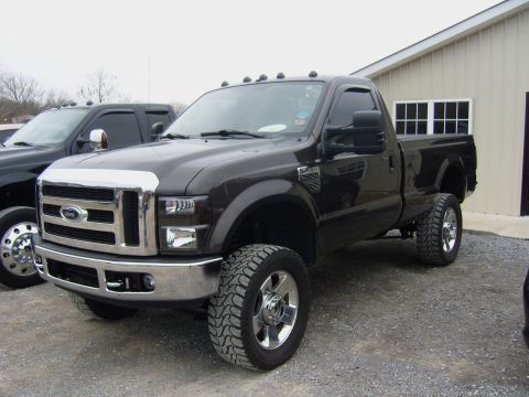 2007 Ford Mustang - A lifted dark brown Ford F-Series truck is parked outside a building, with another truck visible to the left.