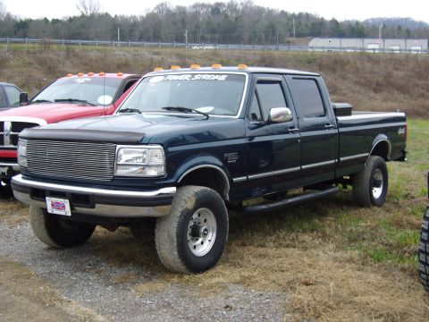 2007 Ford Mustang - A dark blue crew cab pickup truck is parked on a gravel and grass area, with another red truck nearby.