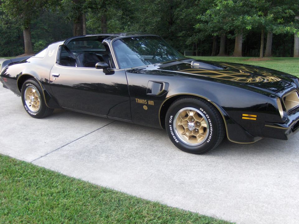 Black 1979 Pontiac Trans Am with gold trim and honeycomb wheels parked on a driveway