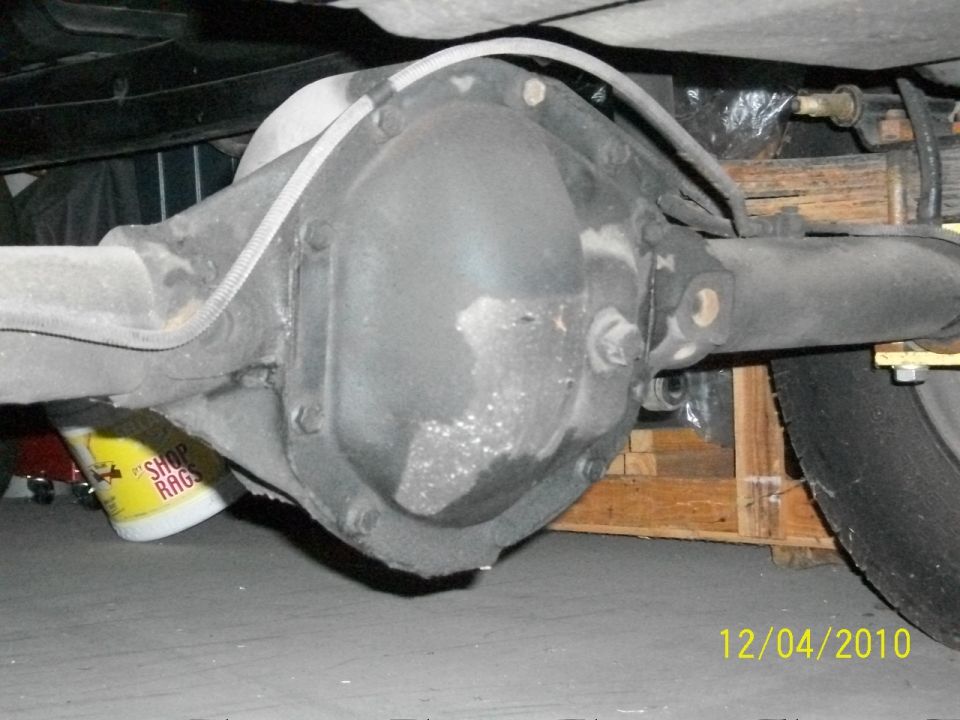 Rear differential assembly with brake line and leaf spring visible. Yellow shop rag on the ground
