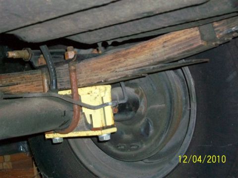 1986 Jeep Wagoneer - This photo shows the underside of a vehicle, focusing on the rear suspension system with leaf springs and a yellow lift block.