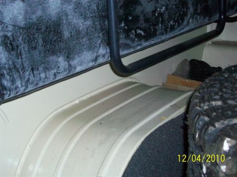 1986 Jeep Wagoneer - The interior of a Jeep shows the ribbed floor of the cargo area and the wheel well, with a spare tire mounted.
