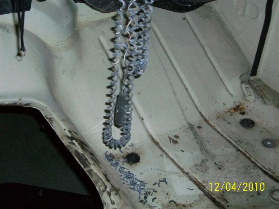 White engine bay with a coiled metal chain hanging, showing rust spots and debris