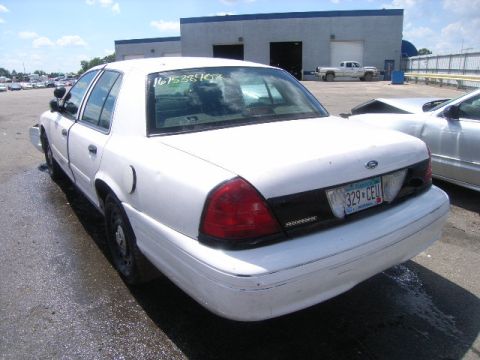 2003 Ford Crown Victoria - A white 2003 Ford Crown Victoria is parked on wet pavement next to another vehicle.