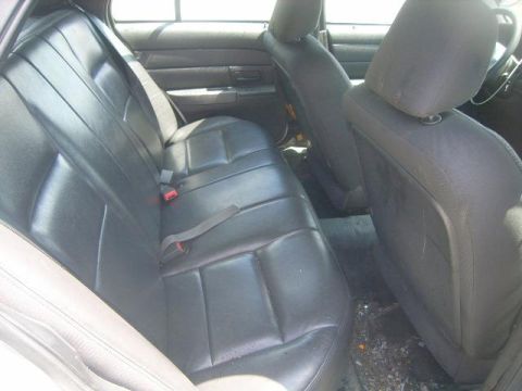 2003 Ford Crown Victoria - The interior of a car shows the rear seats and door panel. The floor is littered with debris.