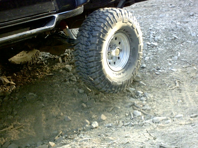 Mud-terrain tire on silver wheel of lifted dark SUV on gravel
