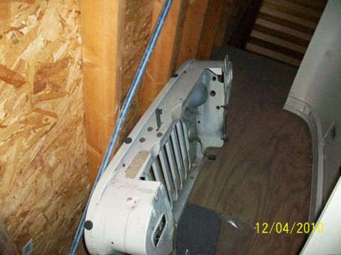 1986 Jeep Wagoneer - A white Jeep grille is stored indoors, leaning against a wall.