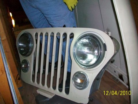 1986 Jeep Wagoneer - A white Jeep CJ grille with vertical slots and round headlights is shown, with a person in blue overalls in the background.