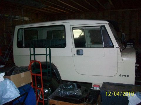 1986 Jeep Wagoneer - A white Jeep is parked inside a garage, surrounded by storage items and equipment.