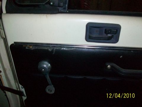 1986 Jeep Wagoneer - Close-up of a car's interior door panel with a manual window crank.