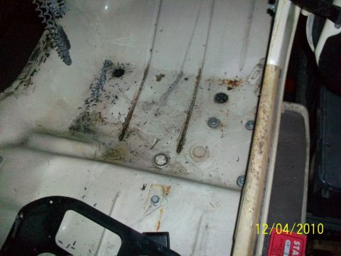 1986 Jeep Wagoneer - The interior floor pan shows signs of rust and debris, with a chain hanging from above.