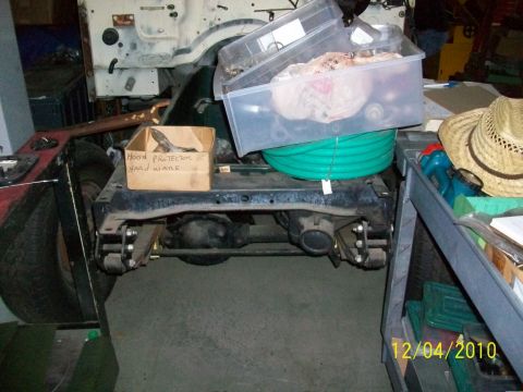 1986 Jeep Wagoneer - The chassis and drivetrain of a Jeep are visible, with storage bins and a straw hat nearby.