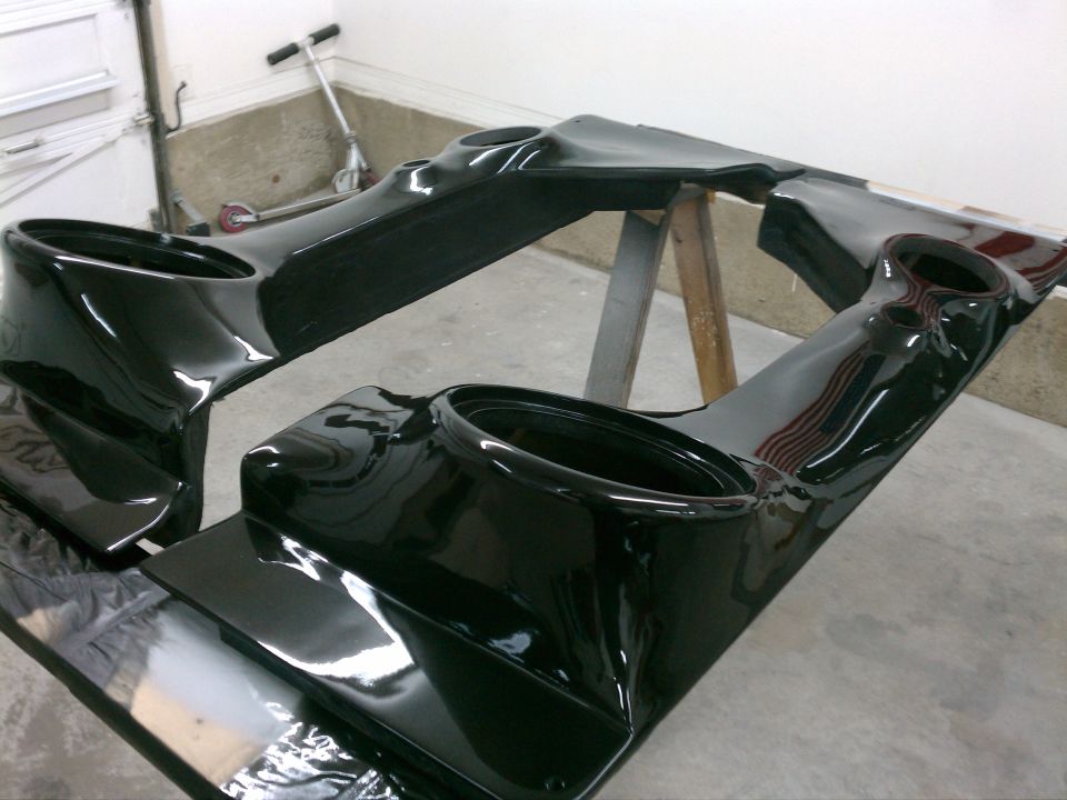 Glossy black fiberglass panels with round cutouts drying on sawhorses in a garage