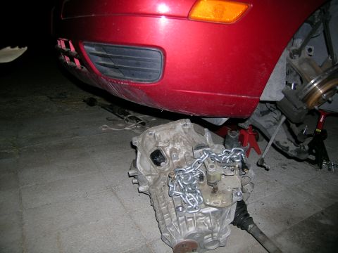 1995 Ford Probe - A red car's front end is raised on jack stands, with its transmission removed and resting on the pavement.